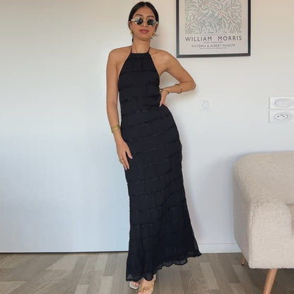 Woman in a black halter neck dress standing indoors against a white wall.