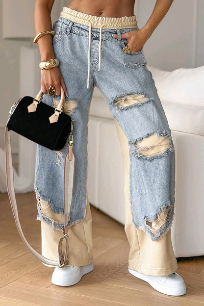 Person wearing ripped jeans with beige accents and holding a black handbag indoors.