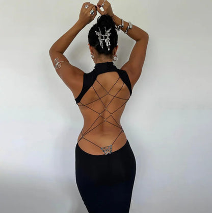 Person wearing a black dress with intricate back design against a plain background